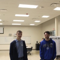 Two students standing next to a block elevator project.